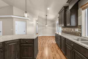 Kitchen with backsplash, dark brown cabinetry, light hardwood / wood-style floors, hanging light fixtures, and lofted ceiling