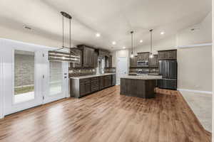 Kitchen featuring dark brown cabinetry, stainless steel appliances, tasteful backsplash, pendant lighting, and a kitchen island