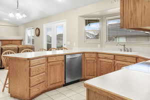 Kitchen featuring kitchen peninsula, stainless steel dishwasher, sink, pendant lighting, and a notable chandelier