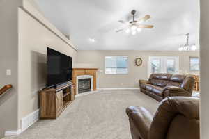 Carpeted living room featuring ceiling fan with notable chandelier and a fireplace