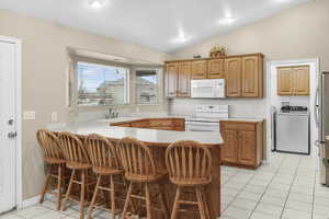 Kitchen with a kitchen bar, white appliances, and kitchen peninsula