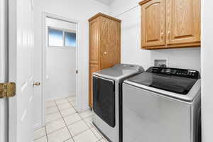 Laundry area featuring cabinets, washing machine and dryer, and light tile patterned floors