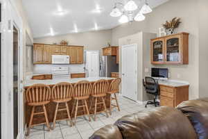 Kitchen featuring range with electric stovetop, lofted ceiling, stainless steel refrigerator with ice dispenser, and light tile patterned floors