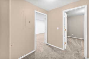 Hall with a textured ceiling, light carpet, and electric panel