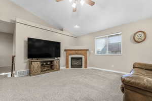 Living room with carpet flooring, vaulted ceiling, ceiling fan, and a tiled fireplace