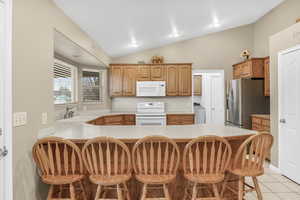 Kitchen with kitchen peninsula, white appliances, sink, light tile patterned floors, and a breakfast bar area