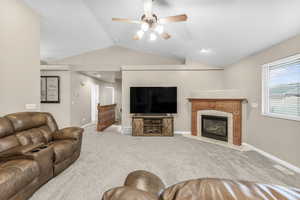 Living room featuring a tile fireplace, carpet floors, vaulted ceiling, and ceiling fan