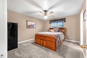 Carpeted bedroom with black fridge and ceiling fan