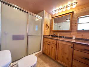 Bathroom with vanity, a shower with door, wooden walls, tile patterned flooring, and toilet