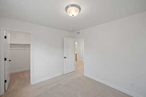 Unfurnished bedroom with light colored carpet, a spacious closet, and a closet