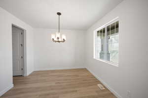 Empty room with light wood-type flooring and a notable chandelier