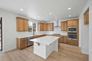 Kitchen featuring wall chimney range hood, decorative backsplash, a kitchen island, light hardwood / wood-style floors, and stainless steel appliances