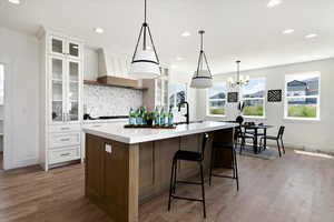 Kitchen with white cabinetry, a large island, sink, decorative light fixtures, and custom exhaust hood