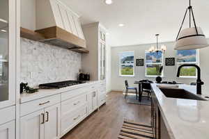 Kitchen featuring light stone counters, custom exhaust hood, stainless steel gas cooktop, sink, and white cabinets