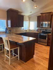 Kitchen with lofted ceiling, tasteful backsplash, light hardwood floors, kitchen peninsula, and stainless steel appliances