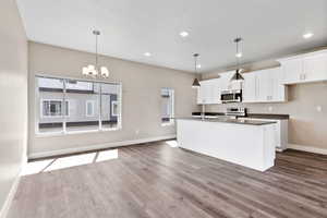 Kitchen with decorative light fixtures, stainless steel appliances, white cabinetry, and light hardwood / wood-style floors