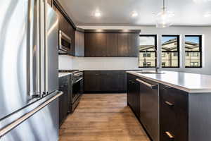 Kitchen featuring high end appliances, sink, hanging light fixtures, light wood-type flooring, and dark brown cabinets