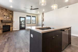 Kitchen with ceiling fan, sink, decorative light fixtures, a center island with sink, and a stone fireplace