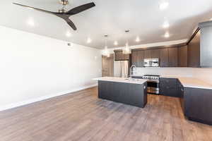 Kitchen with dark brown cabinetry, ceiling fan, premium appliances, decorative light fixtures, and a center island with sink