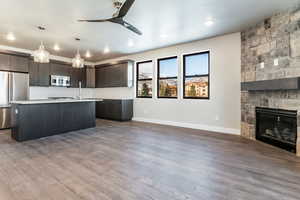 Kitchen featuring a kitchen island with sink, a stone fireplace, decorative light fixtures, dark brown cabinetry, and stainless steel appliances