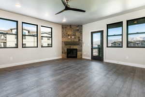 Unfurnished living room featuring a stone fireplace, ceiling fan, and dark wood-type flooring