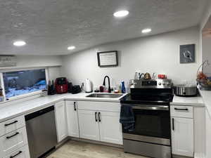 Kitchen with appliances with stainless steel finishes, light lvp flooring, stainless sink and white cabinets