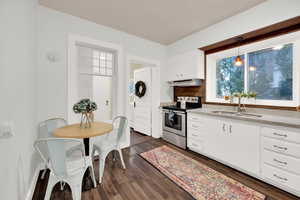 Kitchen with stainless steel electric range, white cabinets, sink, hanging light fixtures, and tasteful backsplash