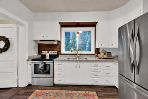 Kitchen with sink, stainless steel appliances, dark hardwood / wood-style flooring, pendant lighting, and white cabinets