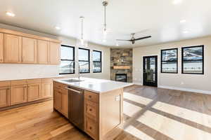 Kitchen featuring a kitchen island with sink, sink, pendant lighting, dishwasher, and a stone fireplace