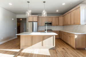 Kitchen featuring sink, light hardwood / wood-style flooring, backsplash, a kitchen island with sink, and appliances with stainless steel finishes