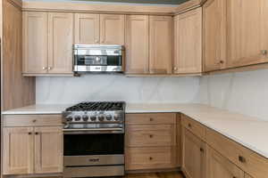 Kitchen featuring stainless steel range, light brown cabinets, and decorative backsplash