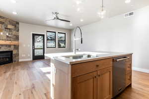 Kitchen featuring dishwasher, a center island with sink, sink, ceiling fan, and a fireplace