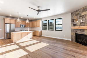 Kitchen featuring stainless steel appliances, a center island with sink, a fireplace, light hardwood / wood-style floors, and hanging light fixtures