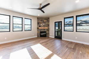 Unfurnished living room featuring a stone fireplace, ceiling fan, and light wood-type flooring