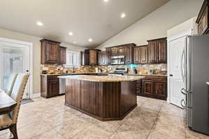 Kitchen featuring dark brown cabinetry, stainless steel appliances, a kitchen island, and lofted ceiling