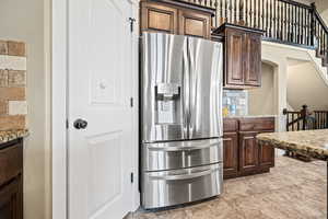 Kitchen with tasteful backsplash, dark brown cabinetry, light stone counters, and stainless steel refrigerator with ice dispenser