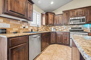 Kitchen featuring light stone countertops, stainless steel appliances, lofted ceiling, dark brown cabinets, and light tile patterned flooring