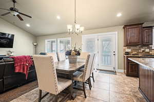 Tiled dining room with ceiling fan with notable chandelier and lofted ceiling