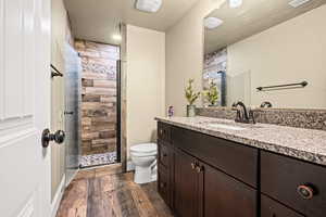 Bathroom featuring hardwood / wood-style floors, a textured ceiling, tiled shower, toilet, and vanity