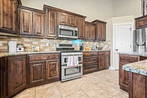 Kitchen with light tile patterned floors, stainless steel appliances, light stone counters, and tasteful backsplash