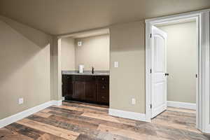 Bar featuring sink, dark brown cabinets, light stone counters, and hardwood / wood-style flooring