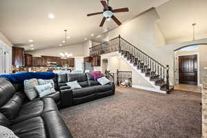 Living room with ceiling fan with notable chandelier, carpet floors, and high vaulted ceiling