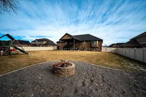 Back of house with a fire pit, a playground, and a yard