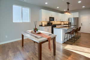 Kitchen with pendant lighting, black appliances, sink, light wood-type flooring, and white cabinetry