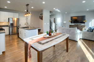 Open Great Room. Kitchen featuring sink, decorative light fixtures, a center island with sink, white cabinets, and appliances with stainless steel finishes