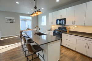 Sliding glass door out to back yard. Kitchen with sink, black appliances, a center island with sink, white cabinetry, and hanging light fixtures