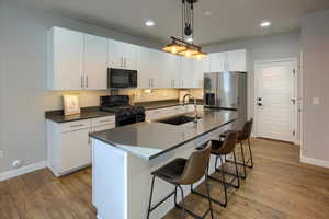 White door out to the garage. Kitchen with a kitchen island with sink, sink, black appliances, pendant lighting, and white cabinets