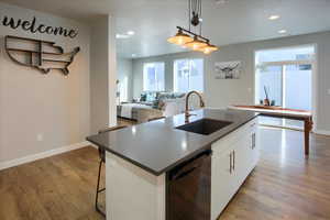 Kitchen with sink, a center island with huge Custom faucet and sink, white cabinets, black dishwasher, and hanging light fixtures