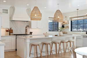 Kitchen with custom exhaust hood, a center island, white cabinets, tasteful backsplash, and decorative light fixtures