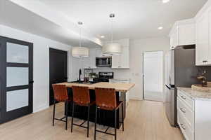 Basement apartment kitchen with white cabinets, a center island with sink, hanging light fixtures, sink, and appliances with stainless steel finishes